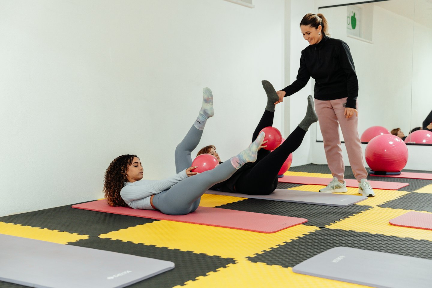 Instruktorka fitness pomaga kobietom w ćwiczeniach pilates na różowych matach.